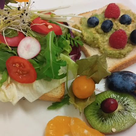A sandwich with greens, a slice of tomato, and a slice of radish. Avocado spread on toast with berries and kiwi.