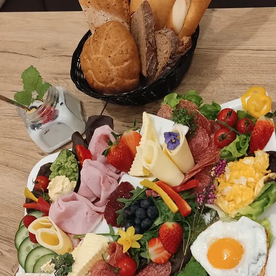 A wooden table displays a large white plate with a variety of foods, including an egg, cheese, strawberries, and bread in a basket.