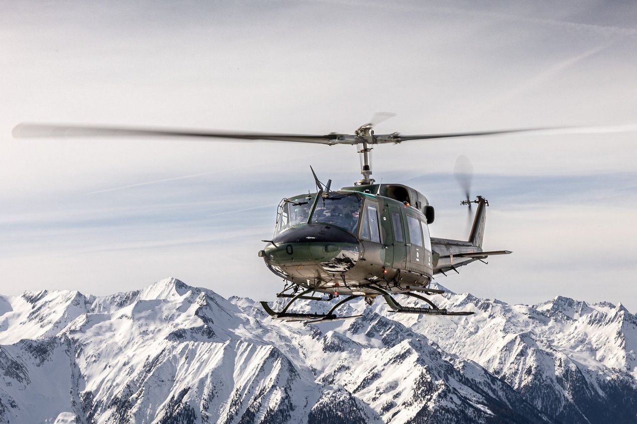 Ein Hubschrauber fliegt über verschneite Berge, die Nummer '0' ist auf der Front sichtbar.