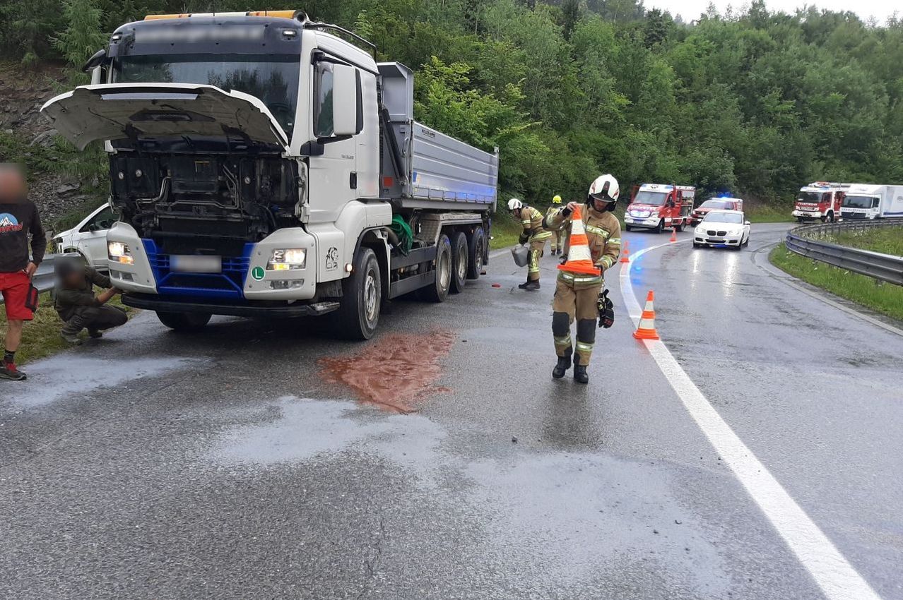 Ein großer Lastwagen mit geöffneter Motorhaube auf einer Straße, bei dem Rettungsdienste einen Unfall bewältigen und Kegel platzieren.