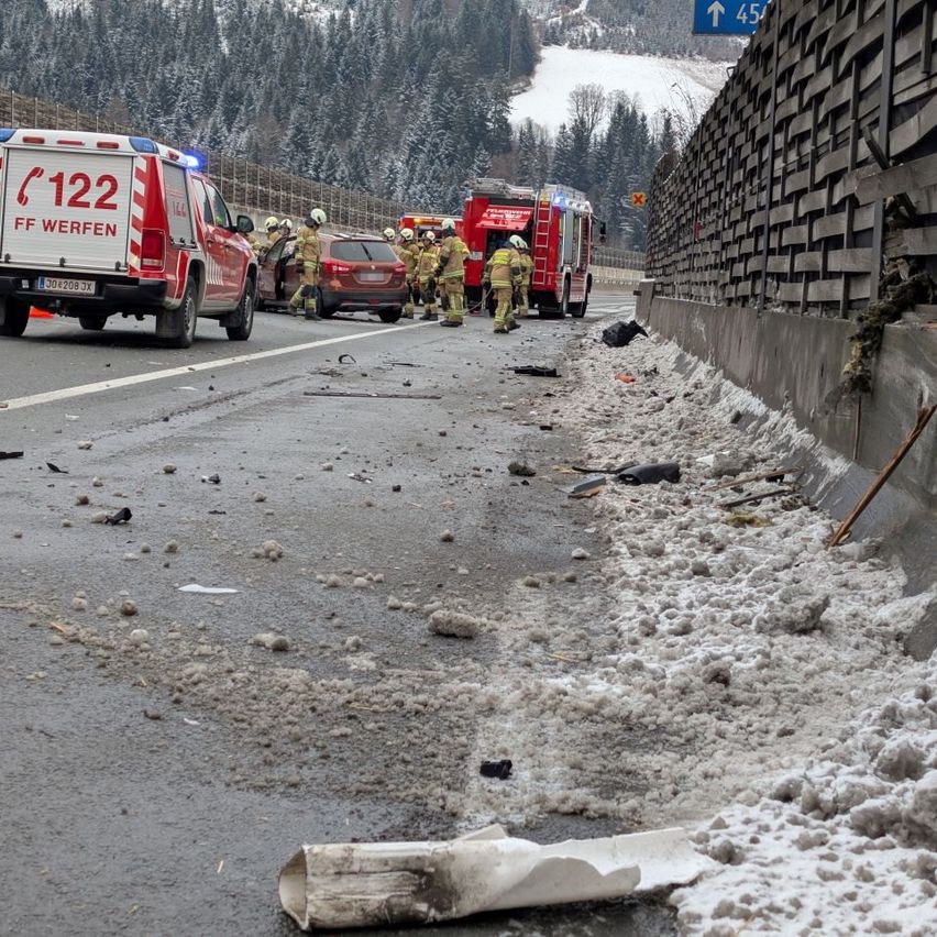 Rettungsfahrzeuge und Feuerwehrleute sind am Straßenrand. Trümmer und Schnee sind verstreut. Im Hintergrund sind mit Schnee bedeckte Berge zu sehen.