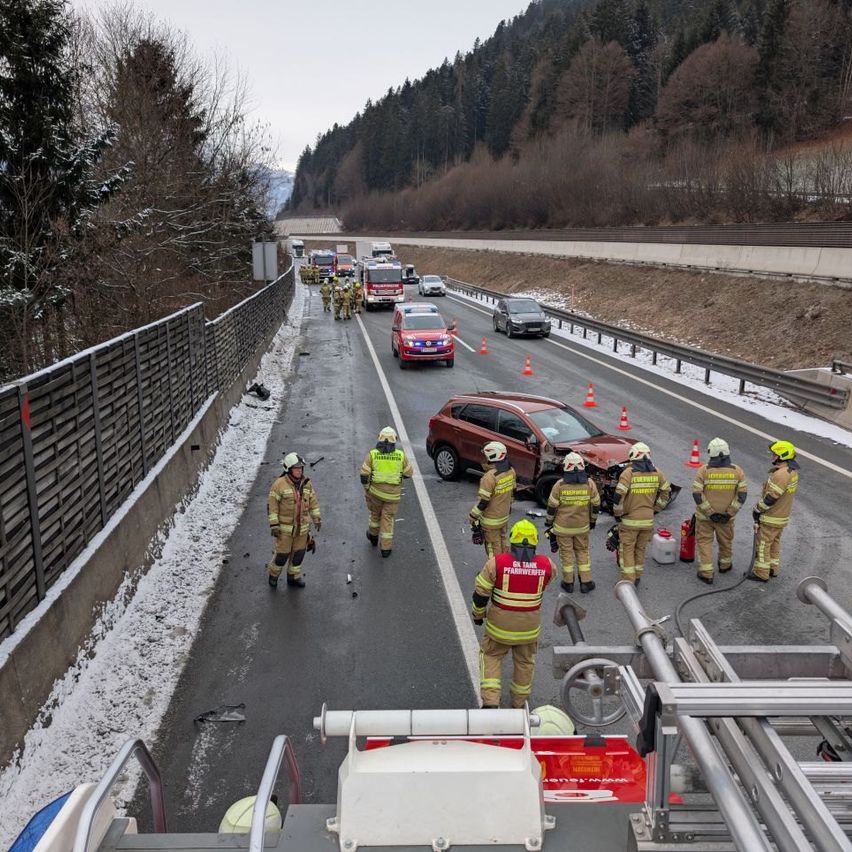 Ein Unfall auf der Autobahn mit mehreren Fahrzeugen hat sich auf einer verschneiten Straße ereignet. Feuerwehrleute und Rettungsdienste sind vor Ort, und Verkehrskegel markieren das Gebiet. Die Fahrzeuge sind gestoppt, und Personal in gelben Uniformen begutachtet die Situation.