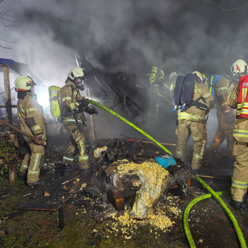 Firefighters in protective gear are battling a blaze. They are using hoses to spray water on the burning structure. The scene is filled with smoke.