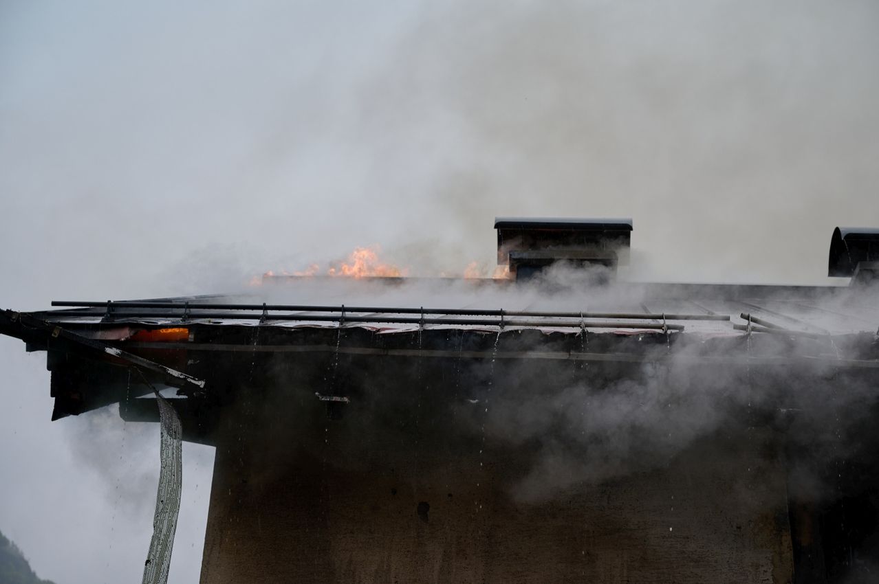 A building's roof is on fire, with smoke and flames visible. The fire seems to be contained to the roof.