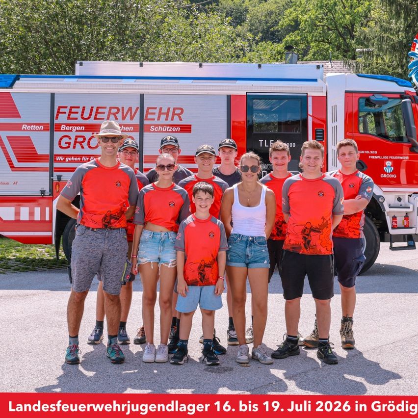 Eine Gruppe von Menschen in passenden roten Shirts posiert für ein Foto vor einem Feuerwehrauto mit den Worten 'Feuerwehr Grodig' darauf. Das Foto wurde am 16. bis 19. Juli 2026 aufgenommen.