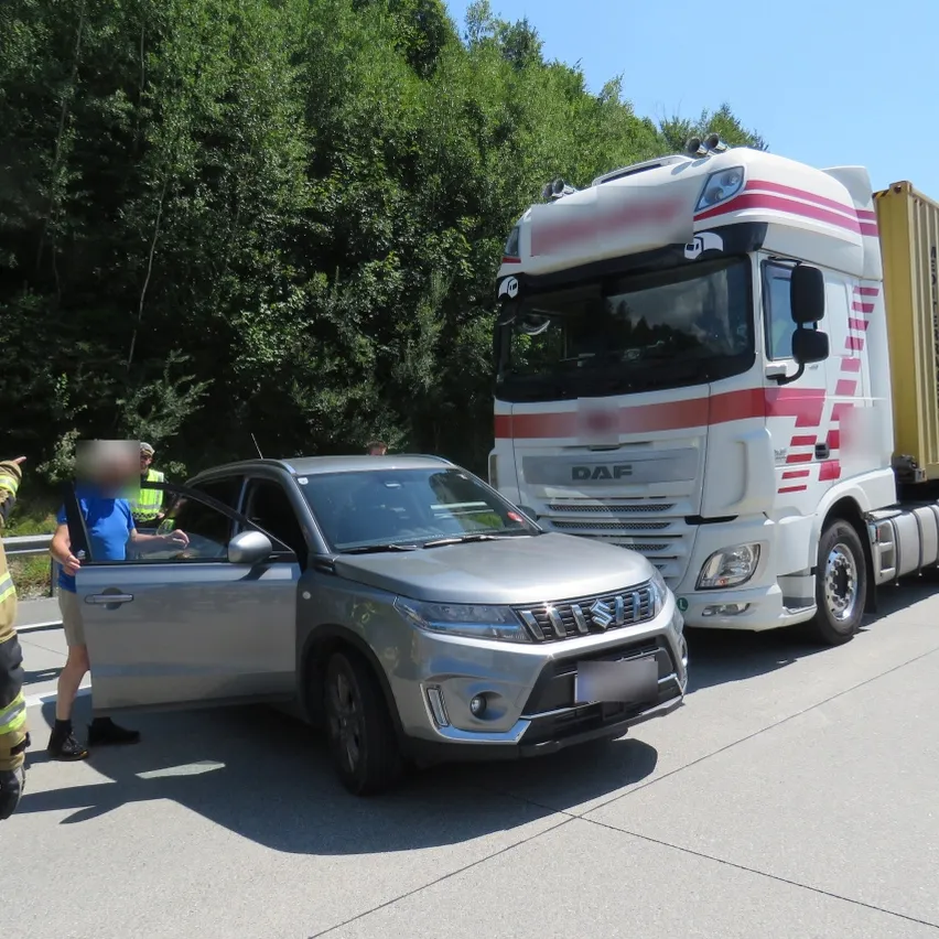 Ein silberner SUV mit offener Tür steht am Straßenrand neben einem DAF-Lkw. Eine Person steht neben der offenen Tür, und ein Verkehrswächter steht hinter dem SUV.
