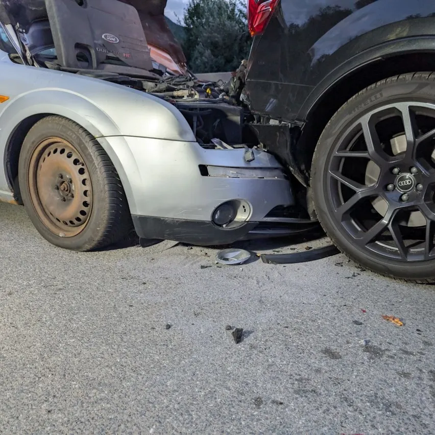 Ein silberner Ford Focus mit offenem Motorhaube und beschädigtem vorderen Stoßfänger ist neben einem schwarzen Audi SUV mit beschädigtem Vorderreifen geparkt.