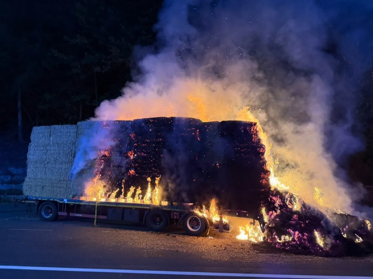 Ein brennender LKW mit Heuballen auf der Rückseite. Das Feuer ist intensiv, mit Rauch und Flammen, die die Heuballen umschließen.