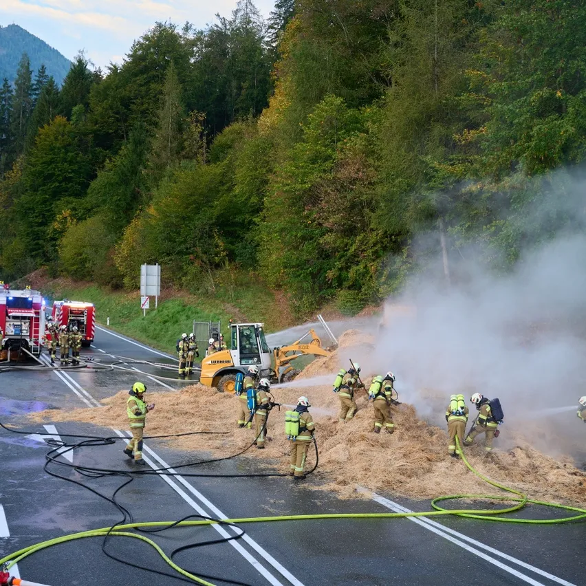 Eine Gruppe von Feuerwehrleuten ist auf einer Straße und spritzt Wasser auf einen Haufen Heu.