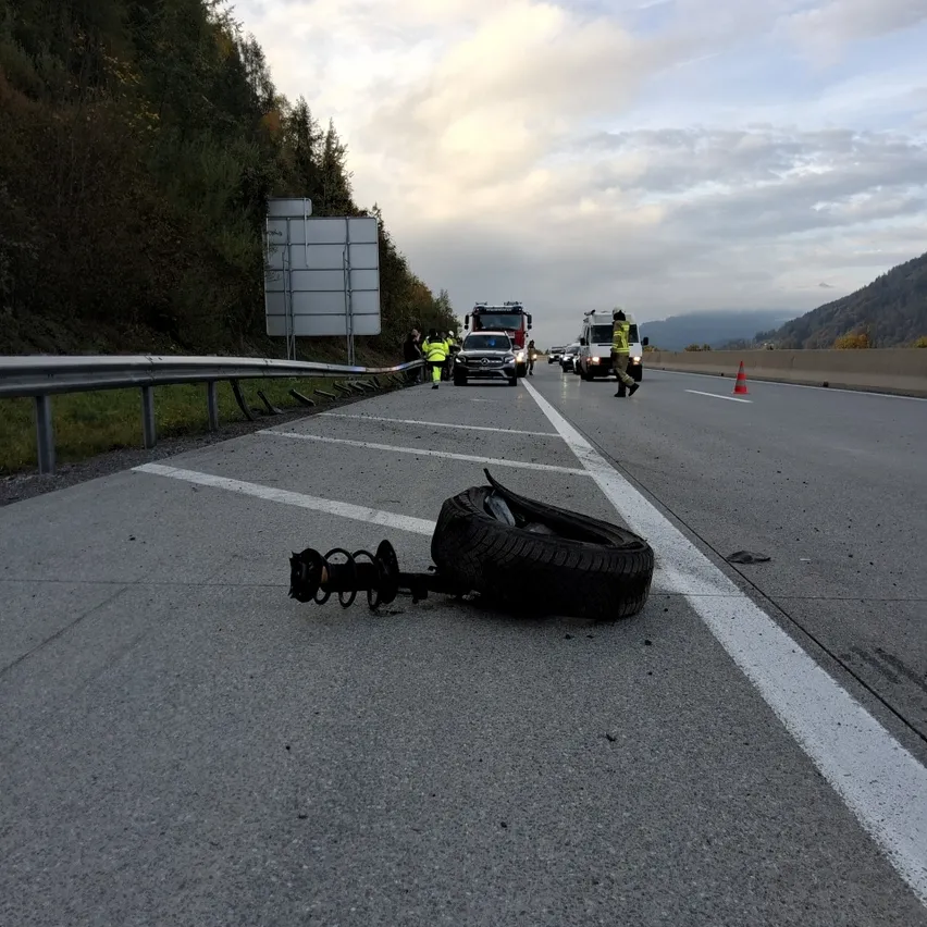 Eine Autobahn mit einem platten Reifen auf der Straße, geparkten Rettungsfahrzeugen an der Seite und Leuten, die herumstehen.