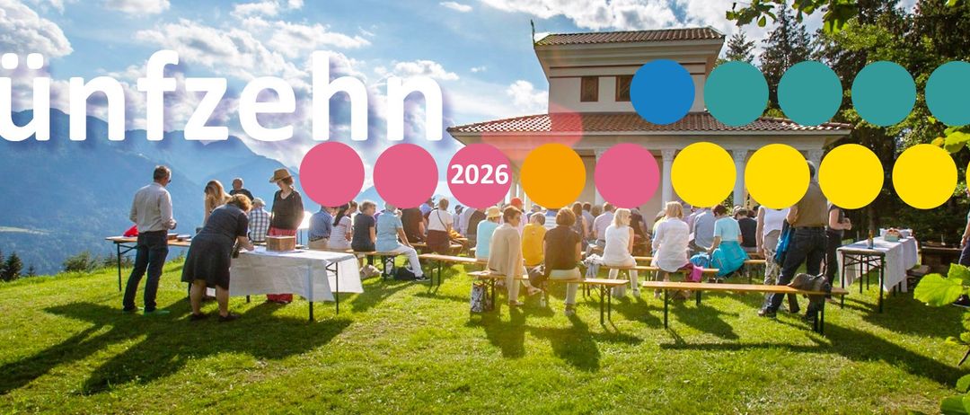 Viele Menschen versammeln sich in einem Park unter einem klaren blauen Himmel. Sie sitzen auf Bänken um Tische herum, auf einem Tisch steht eine Kiste. Ein Gebäude mit einem Ziegeldach befindet sich hinter ihnen. Das Wort 'ehn' und das Jahr 2026 sind im Vordergrund.