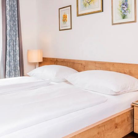 Ein Schlafzimmer mit einem Doppelbett und weißer Bettwäsche. Der Raum verfügt über ein hölzerne Kopfteil und eine Lampe auf dem Nachttisch. Drei gerahmte Bilder schmücken die Wand.