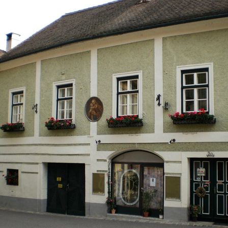 Ein Haus mit einem Strohdach und weißen Wänden hat zwei schwarze Türen und zwei Fenster mit roten Blumen auf den Fensterbänken.