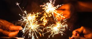 Eine Person hält brennende Wunderkerzen in beiden Händen, wobei das Gesicht einer Frau im Hintergrund verschwommen ist.