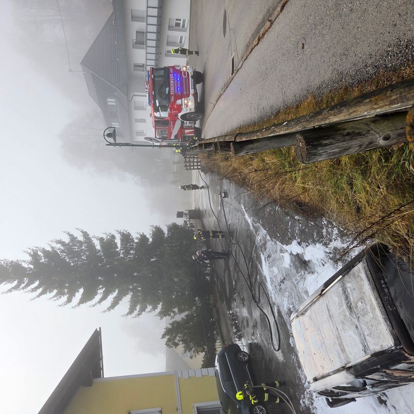 Ein Feuerwehrfahrzeug ist am Straßenrand in einem nebligen Umfeld geparkt. Mehrere Feuerwehrleute arbeiten am Straßenrand, und einige von ihnen stehen in der Nähe des Autos.