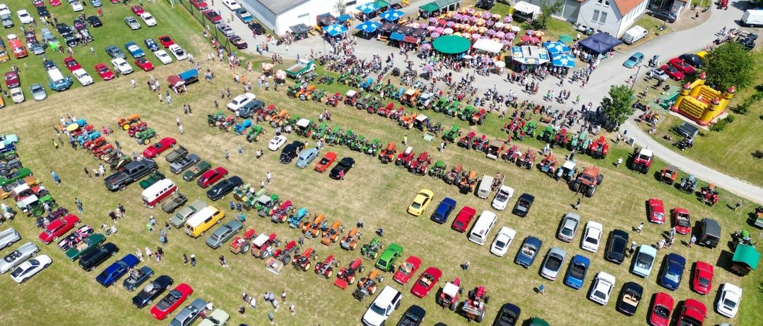 Eine Luftaufnahme einer großen Versammlung von Oldtimern und Traktoren, die auf einem Feld geparkt sind, mit vielen Menschen, die herumlaufen.