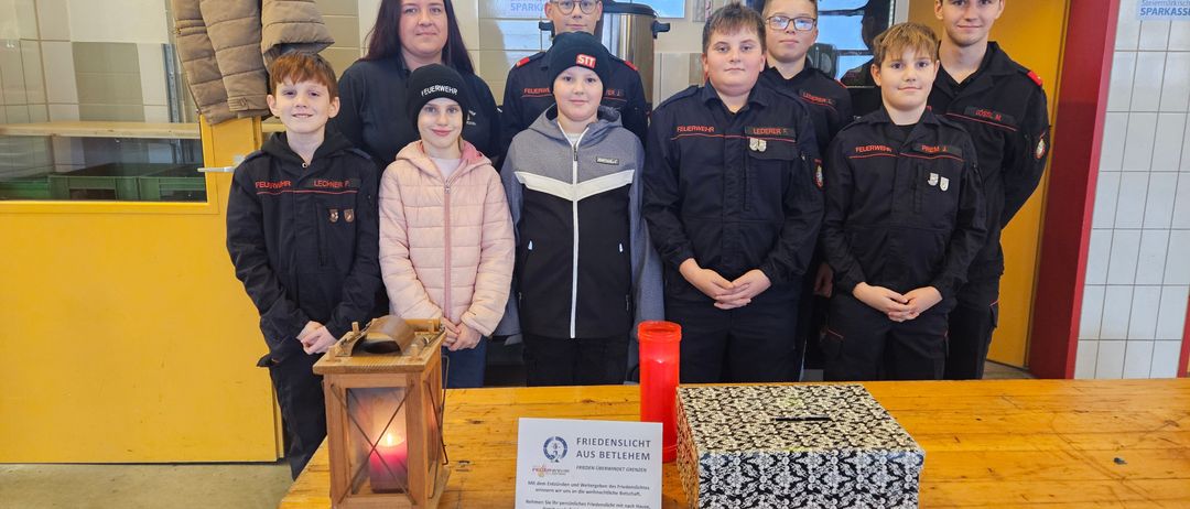 Mehrere junge Menschen in Uniformen stehen hinter einem Tisch und lächeln. Ein Laterne und eine Spendenbox stehen auf dem Tisch.