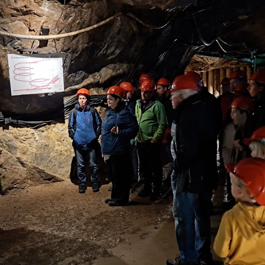 Eine Gruppe von Personen in einem Tunnel mit Schutzhelmen, eine Person mit einer Taschenlampe und einem Schild an der Wand.