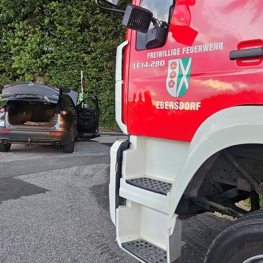 A red fire truck from Ebersdorf is parked on the side of the road with its back door open, next to a black car with its trunk open.