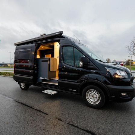 Ein schwarzer Van mit offener Tür steht am Straßenrand. Das Innere ist sichtbar und zeigt einen kleinen Holzschrank.