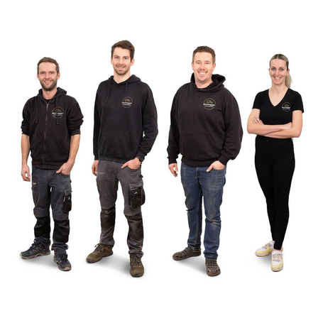 Vier Menschen stehen in einer Reihe, alle tragen schwarze Hoodies und Hosen. Der Mann links hat einen Reißverschluss-Hoodie, während der Mann in der Mitte eine Kapuzenjacke trägt. Der Mann rechts trägt Jeans. Die Frau rechts trägt ein schwarzes T-Shirt und Turnschuhe.