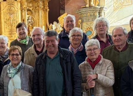 Eine Gruppe von Menschen posiert für ein Foto in einer Kirche mit kunstvollen goldenen Altären und Statuen im Hintergrund.