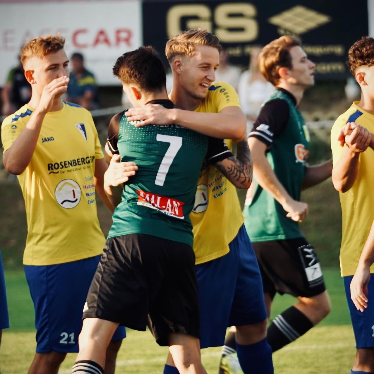 Fußballspieler in gelben und grünen Trikots feiern auf dem Spielfeld. Der Spieler in Grün hat die Nummer 7 auf seinem Trikot.