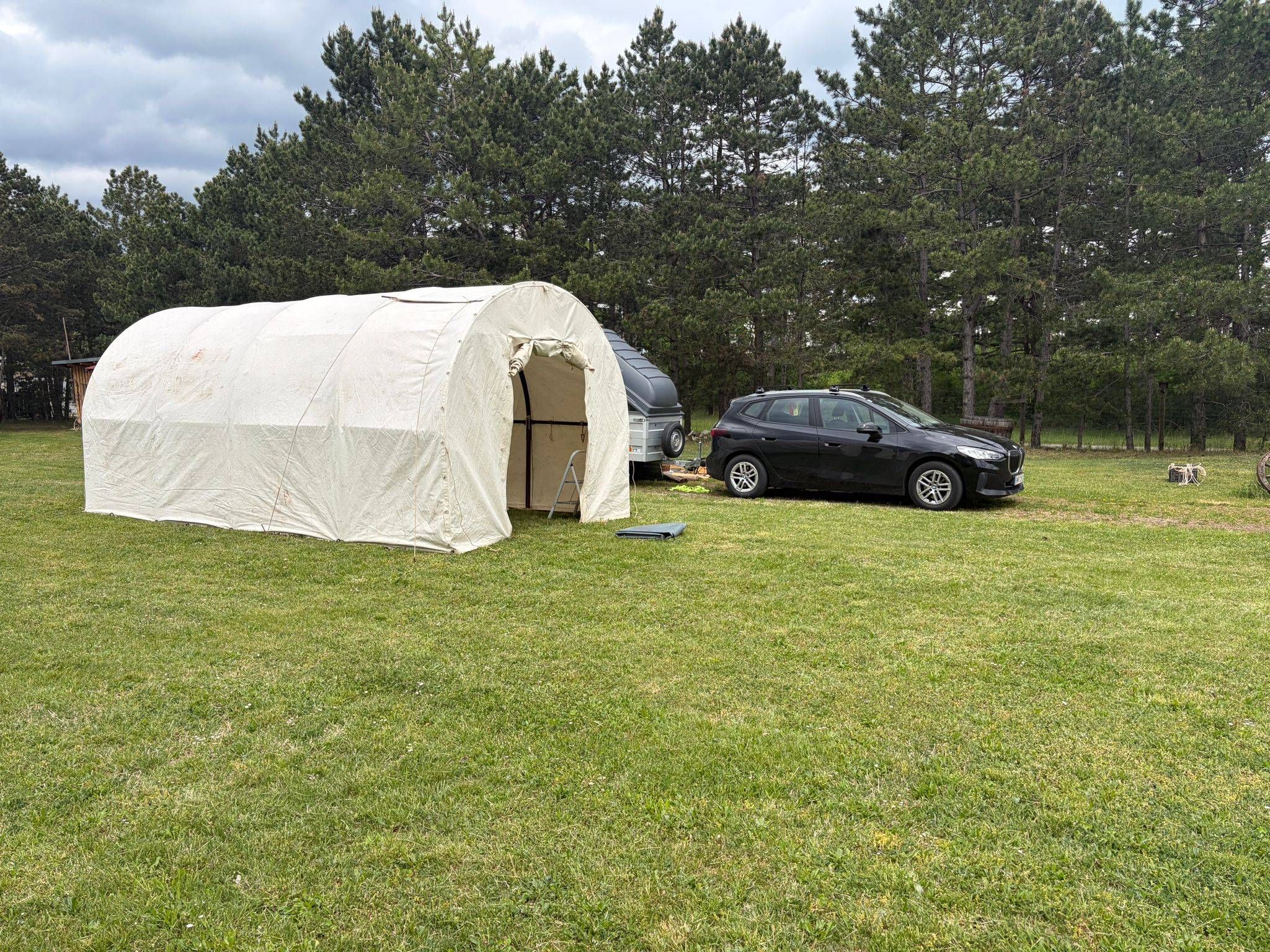 Ein schwarzer SUV ist auf einem Rasenfeld geparkt, mit einem großen weißen Zelt und einem Anhänger. Bäume im Hintergrund.