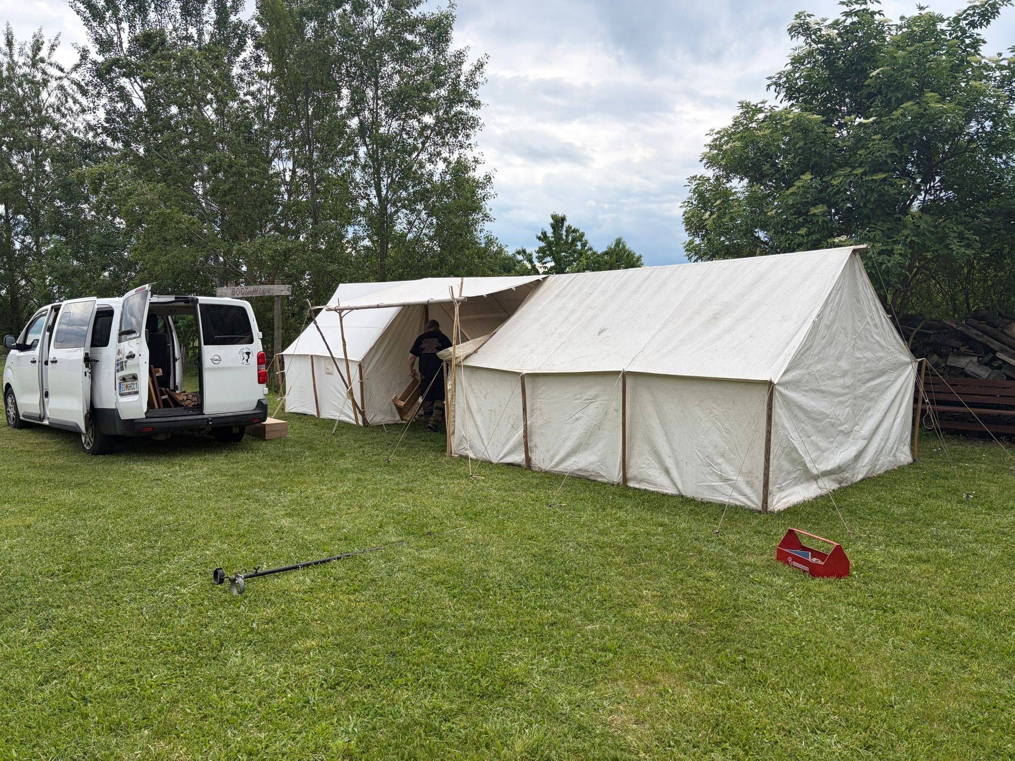 Zwei große weiße Zelte sind auf einem Rasen aufgebaut. Eine Person arbeitet am rechten Zelt. Ein Van ist links geparkt.