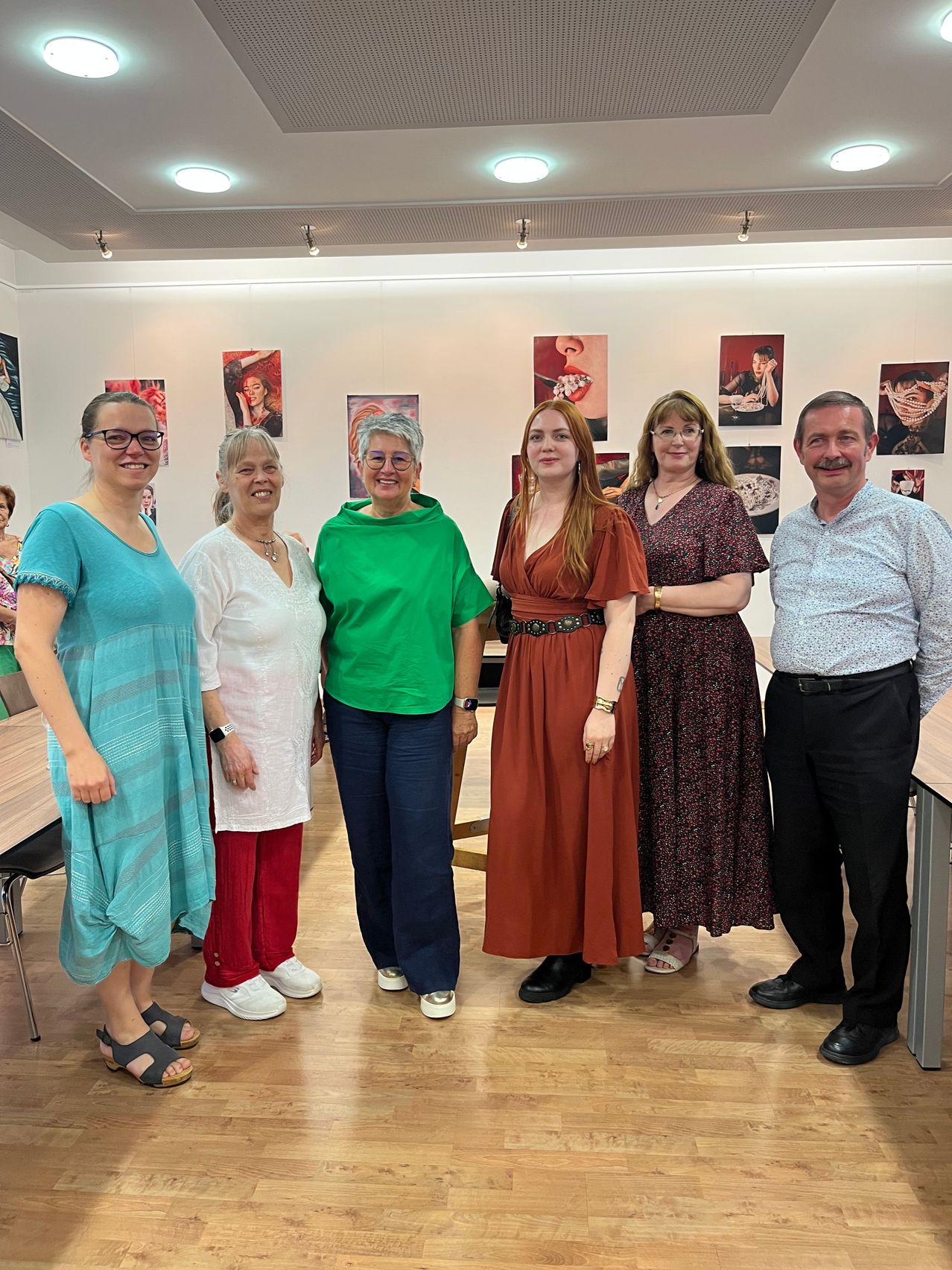 Eine Gruppe von sieben Personen, darunter vier Frauen und drei Männer, steht lächelnd in einer Kunstgalerie zusammen und posiert für ein Foto. Hinter ihnen hängen verschiedene Gemälde an der Wand.
