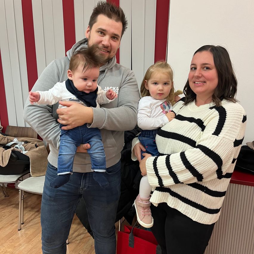 Ein Mann und eine Frau posieren mit zwei kleinen Kindern. Der Mann hält ein Baby und die Frau ein Kleinkind. Sie lächeln.