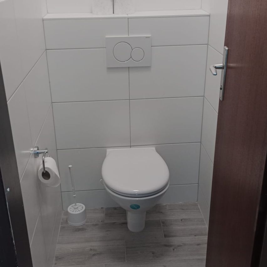 Ein sauberes, weißes, modernes Badezimmer mit gefliesten Wänden, einer Toilette und einem Toilettenpapierhalter an der Wand.