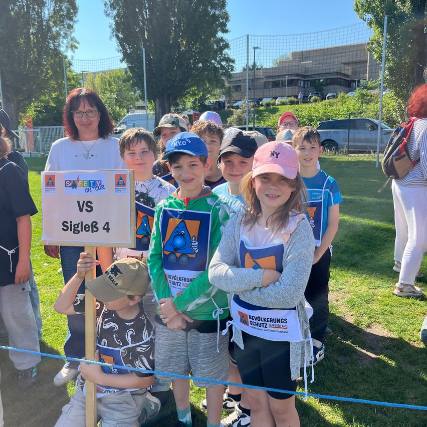 Group of children in casual clothes posing for a photo with a sign reading Safety on Tour VS Single 4.