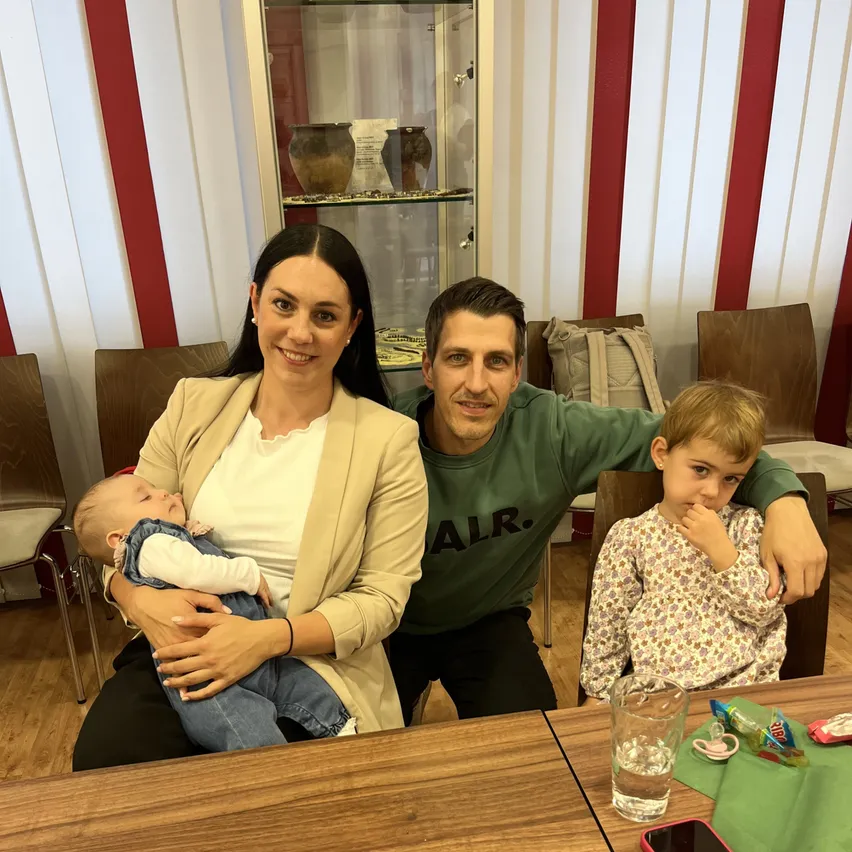 Familie mit Kindern in einem Raum mit Vitrine und Stühlen.
