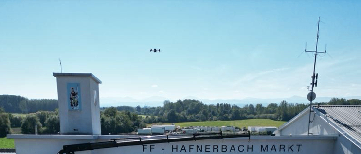 Eine Feuerwehrstation mit dem Namen FF - Hafnerbach Markt. Mehrere Feuerwehrfahrzeuge sind davor geparkt. Der Himmel ist klar und blau.