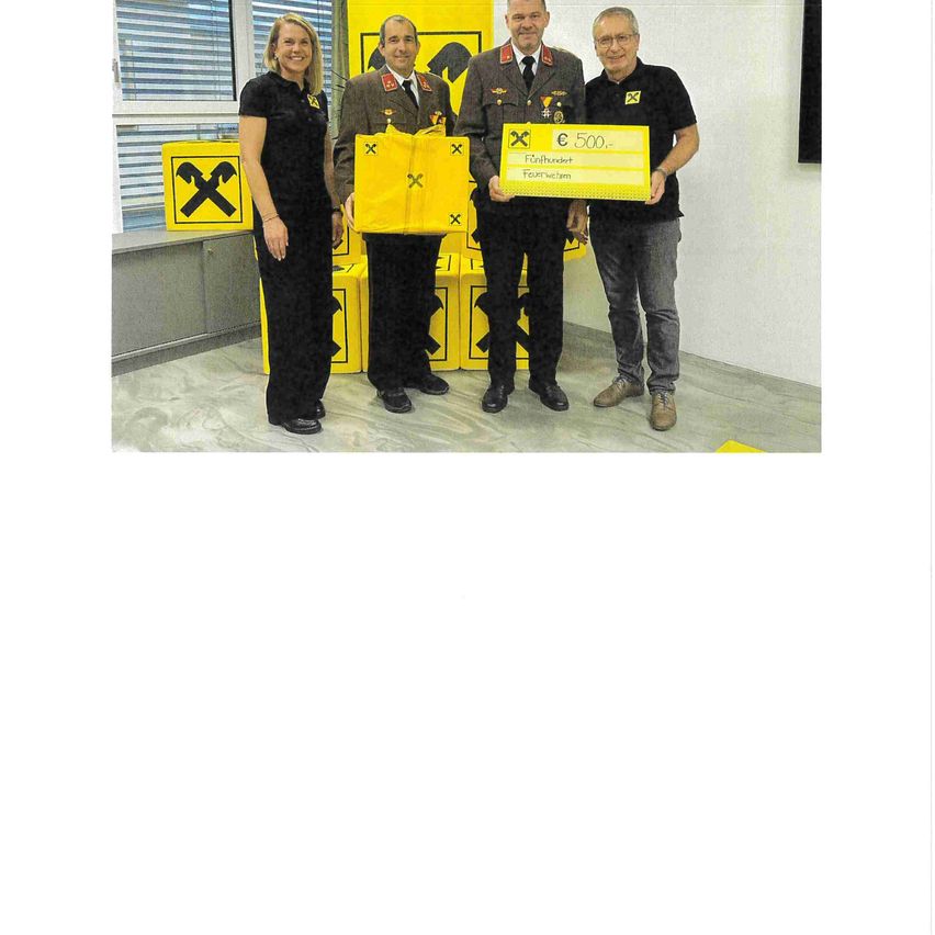 Fünf Personen stehen in einem Raum, zwei halten eine gelbe Tasche mit einem 500 € Spendenscheck. Der Raum hat gelbe Boxen mit einem 'X'-Symbol.