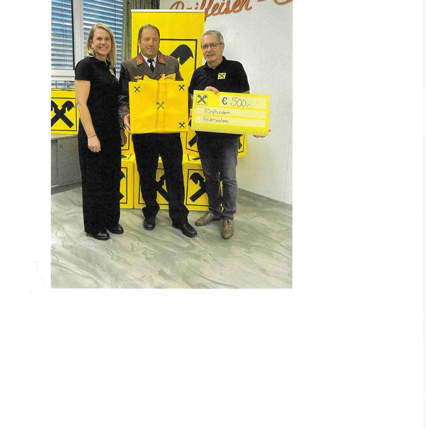 Drei Personen stehen vor einem gelben Hintergrund. Die beiden Männer halten ein gelbes Objekt mit einem Scheck darauf. Die Frau steht neben einem der Männer.