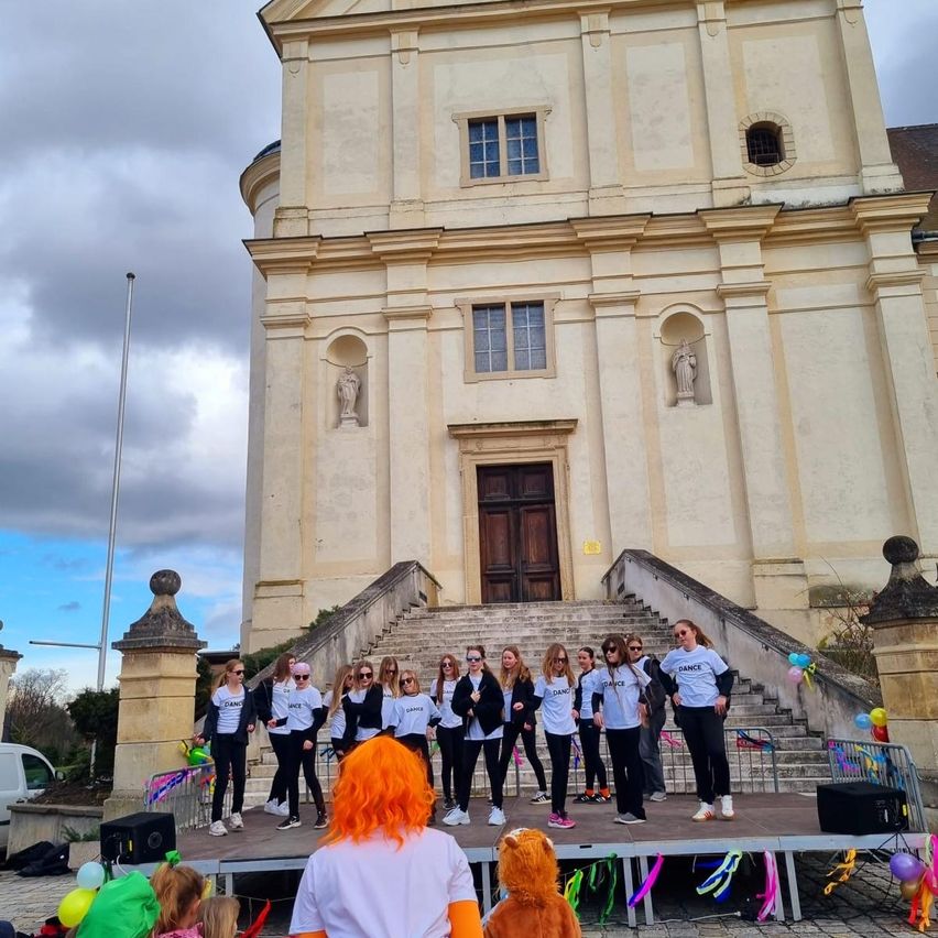 A group of women with orange hair stands on a stage in front of a church, wearing matching outfits and posing for a photo.