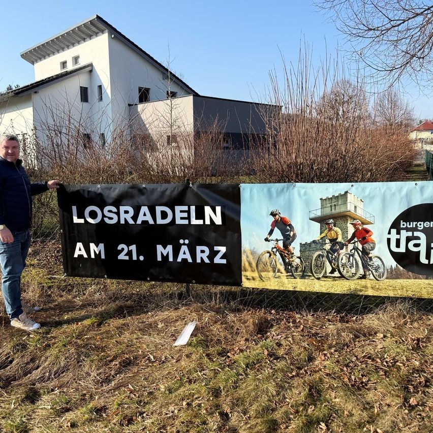 A man holds a banner advertising 'Losradeln' on March 21, in front of a house and a banner featuring people on bikes.