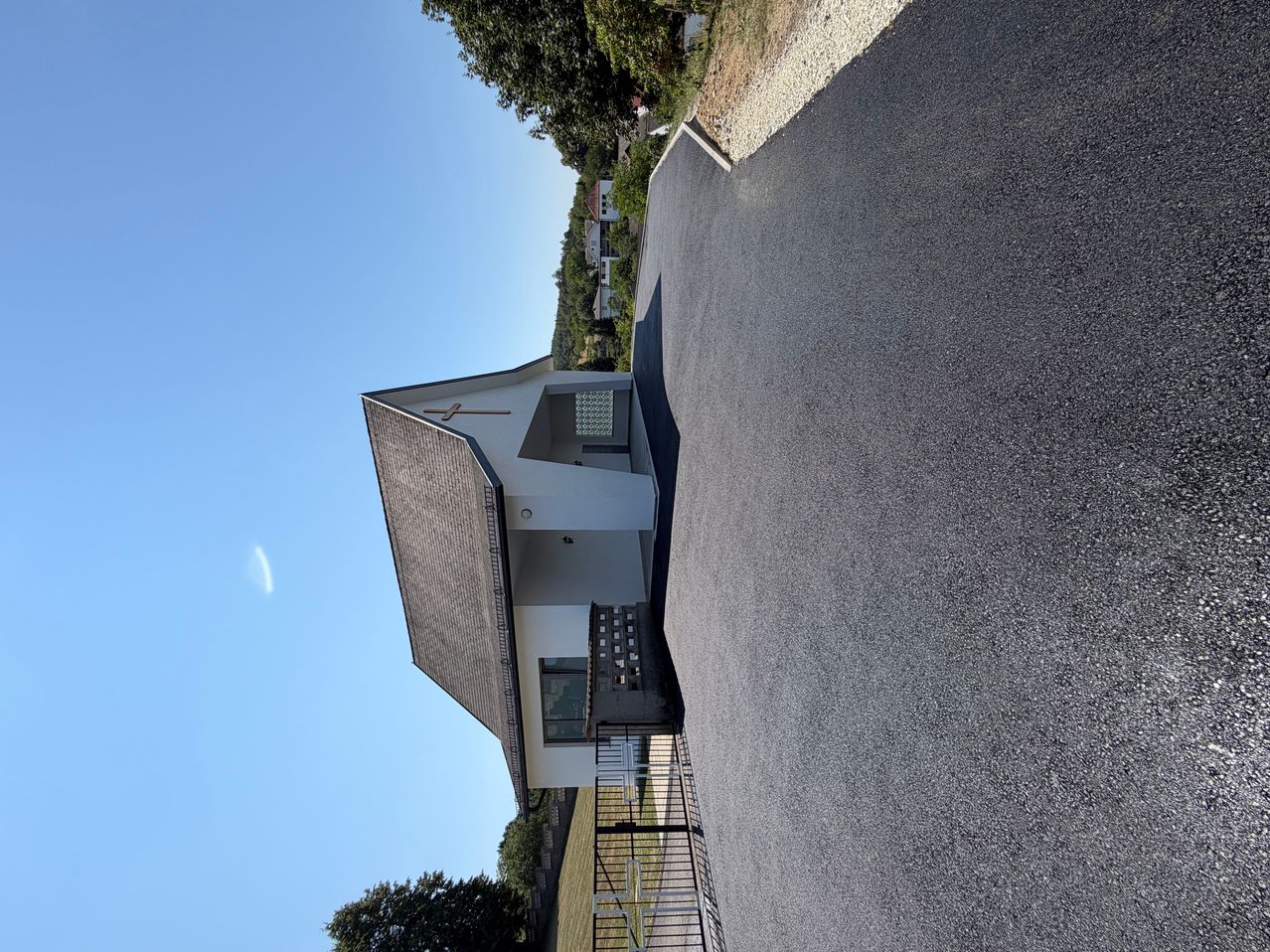 Kirche mit Kreuz und weißer Fassade, daneben asphaltierte Fläche und Grünanlage
