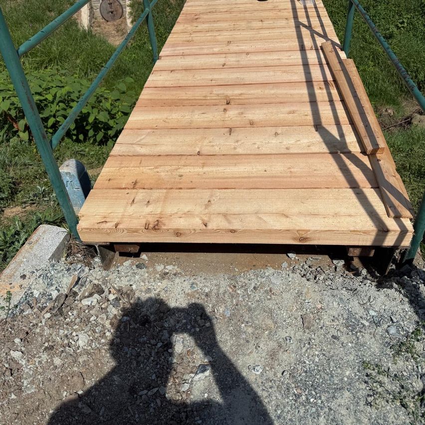 Eine Holzbrücke mit grünen Geländern wird gebaut. Die Brücke wird von Kies und Beton gestützt.