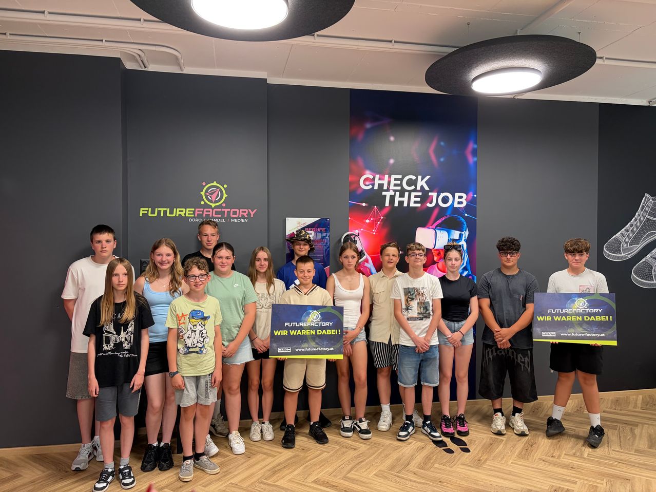 Eine Gruppe von Kindern und Jugendlichen posiert für ein Foto in einem Raum mit einem Banner, das Check The Job und ein Schild mit Future Factory steht.