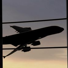 Die Silhouette eines großen Flugzeugs vor einem Himmel in der Dämmerung, durch eine Glaswand gesehen.