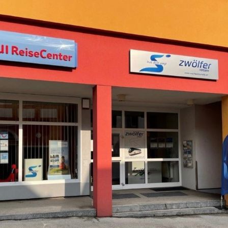 Der Eingang des TUI ReiseCenter-Gebäudes zeigt ein blaues Schild mit weißen Buchstaben, auf dem 'TUI ReiseCenter' steht. Über dem Eingang befindet sich ein weiteres Schild mit dem Wort 'zwolfer' in Blau.