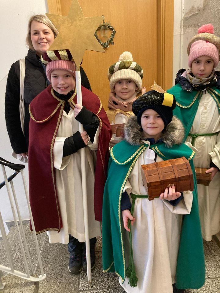 Mehrere Kinder in Weihnachtskostümen posieren für ein Foto, eines hält eine Holzkiste und ein anderes eine Sterne.