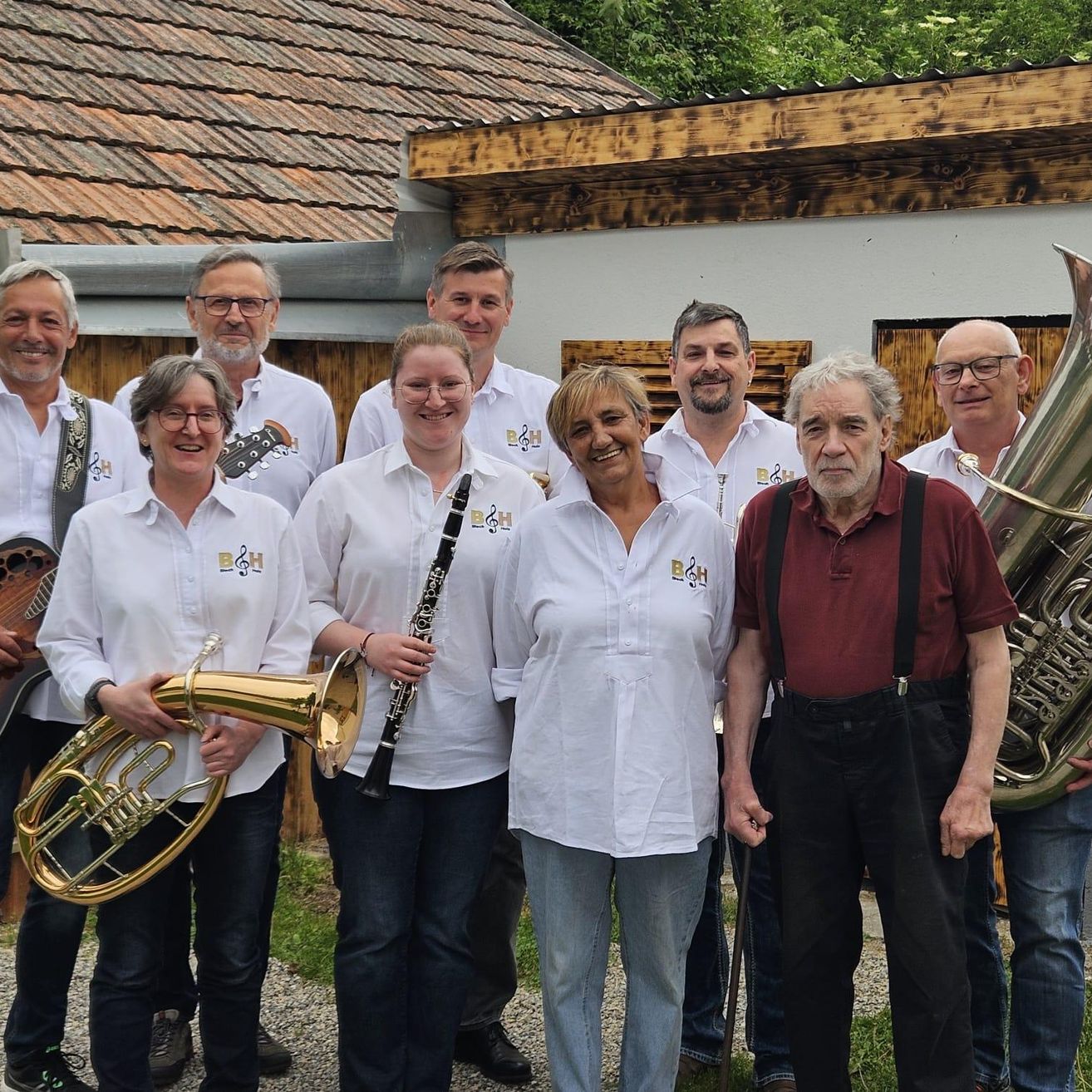 Eine Gruppe von Musikern posiert für ein Foto vor einem Haus. Sie halten Musikinstrumente wie Tuba, Klarinette und Gitarre.