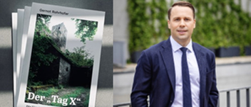 Ein Mann in Anzug und Krawatte steht neben einem Metallzaun, mit einem Flyer für 'Der Tag X' an der Wand dahinter. Der Flyer zeigt ein rustikales Gebäude mit viel Grün.