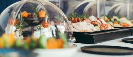 Ein Tisch ist mit verschiedenen glasüberdachten Gerichten gedeckt. Eines hat Fleisch und Gemüse, ein anderes Salat mit Gurken und Tomaten.