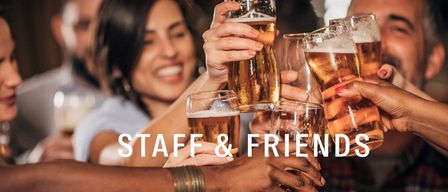 A group of friends and staff raising glasses of beer together, smiling and laughing in a lively atmosphere.
