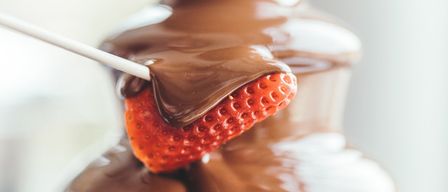A strawberry is dipped into a chocolate fountain, showcasing the melting chocolate around the fruit.